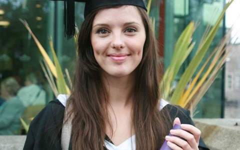 Cheryl Appleby wearing a graduation gown and holding a certificate tube thing