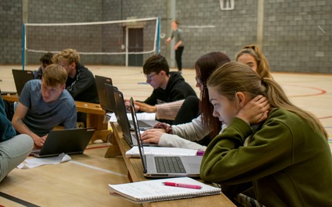 students at laptops in a gym hall