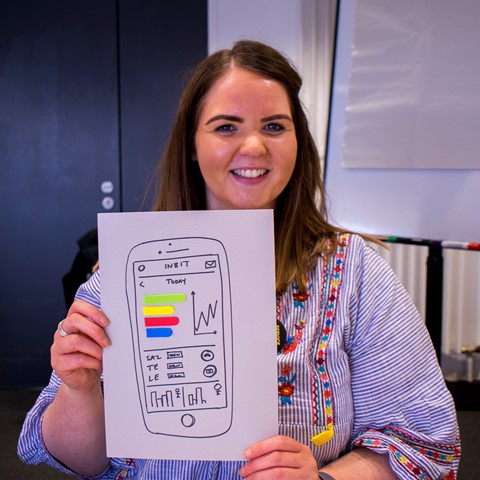Lady holding up a design for a smartphone app she made using service design tools