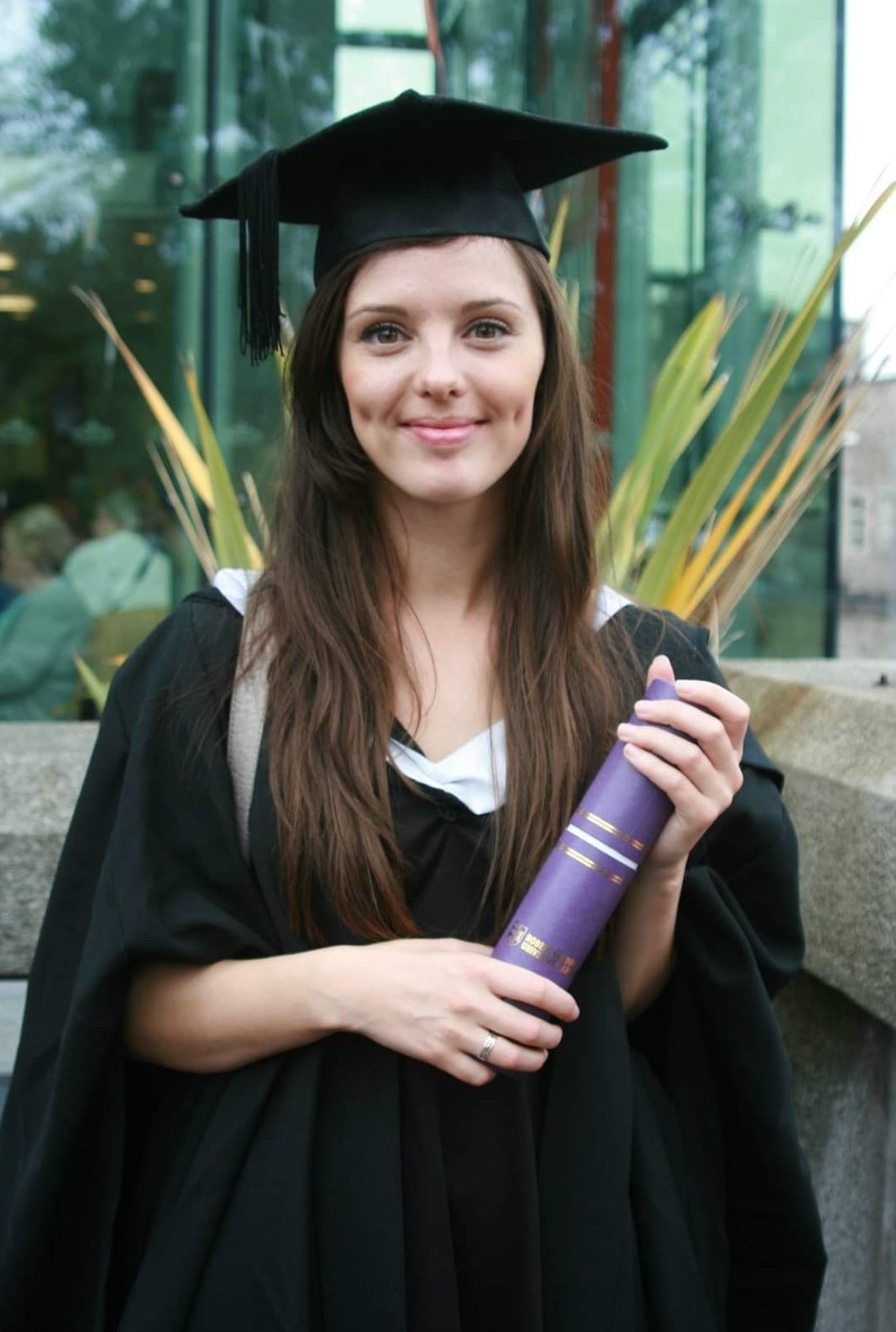 Cheryl Appleby wearing a graduation gown and holding a certificate tube thing