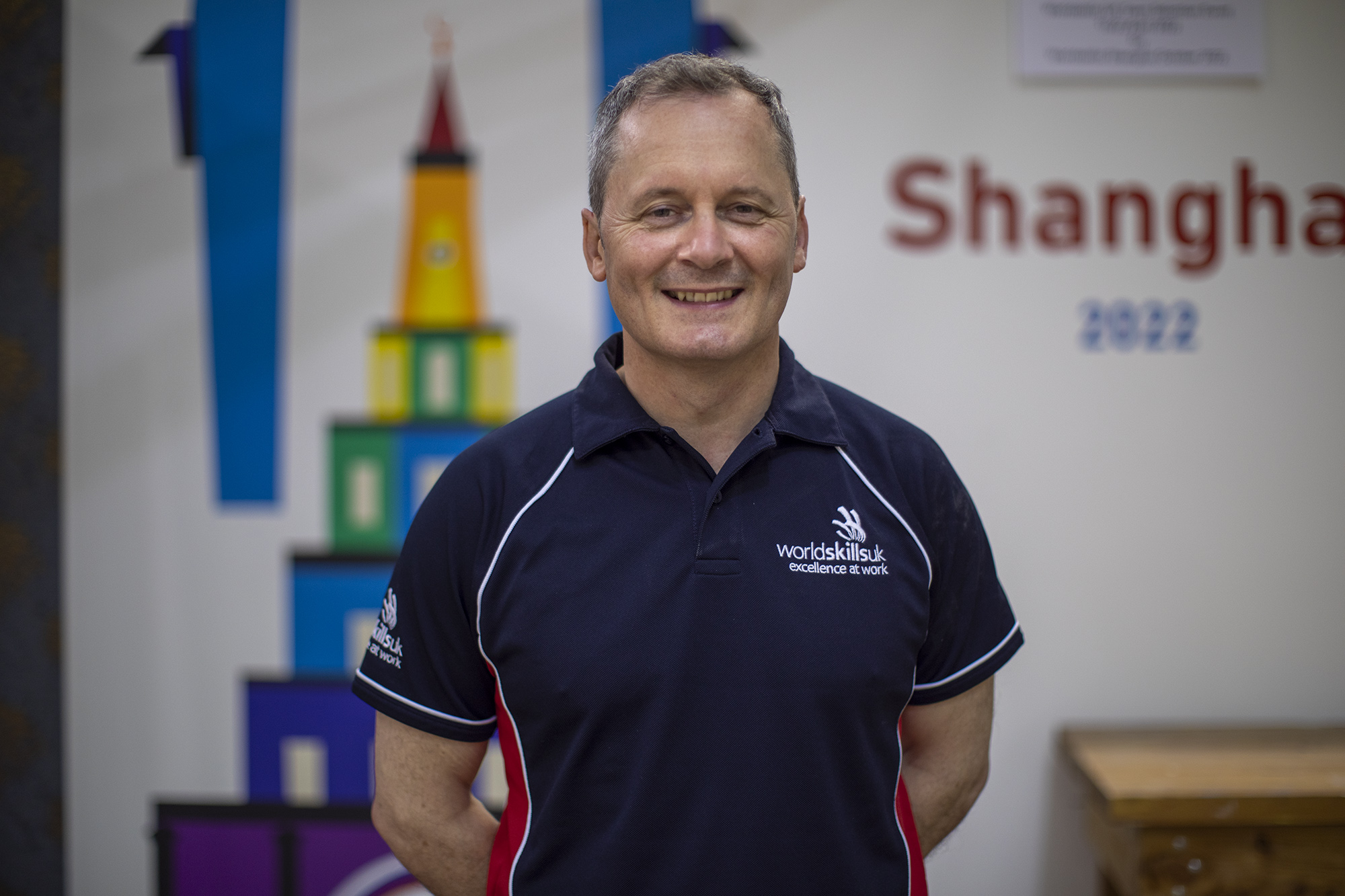 Lecturer Mike Swan posing behind 2022 world skills shanghai banner