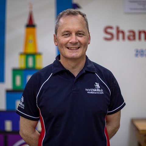 Lecturer Mike Swan posing behind 2022 world skills shanghai banner