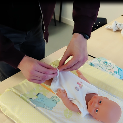 Student putting clothes on model baby