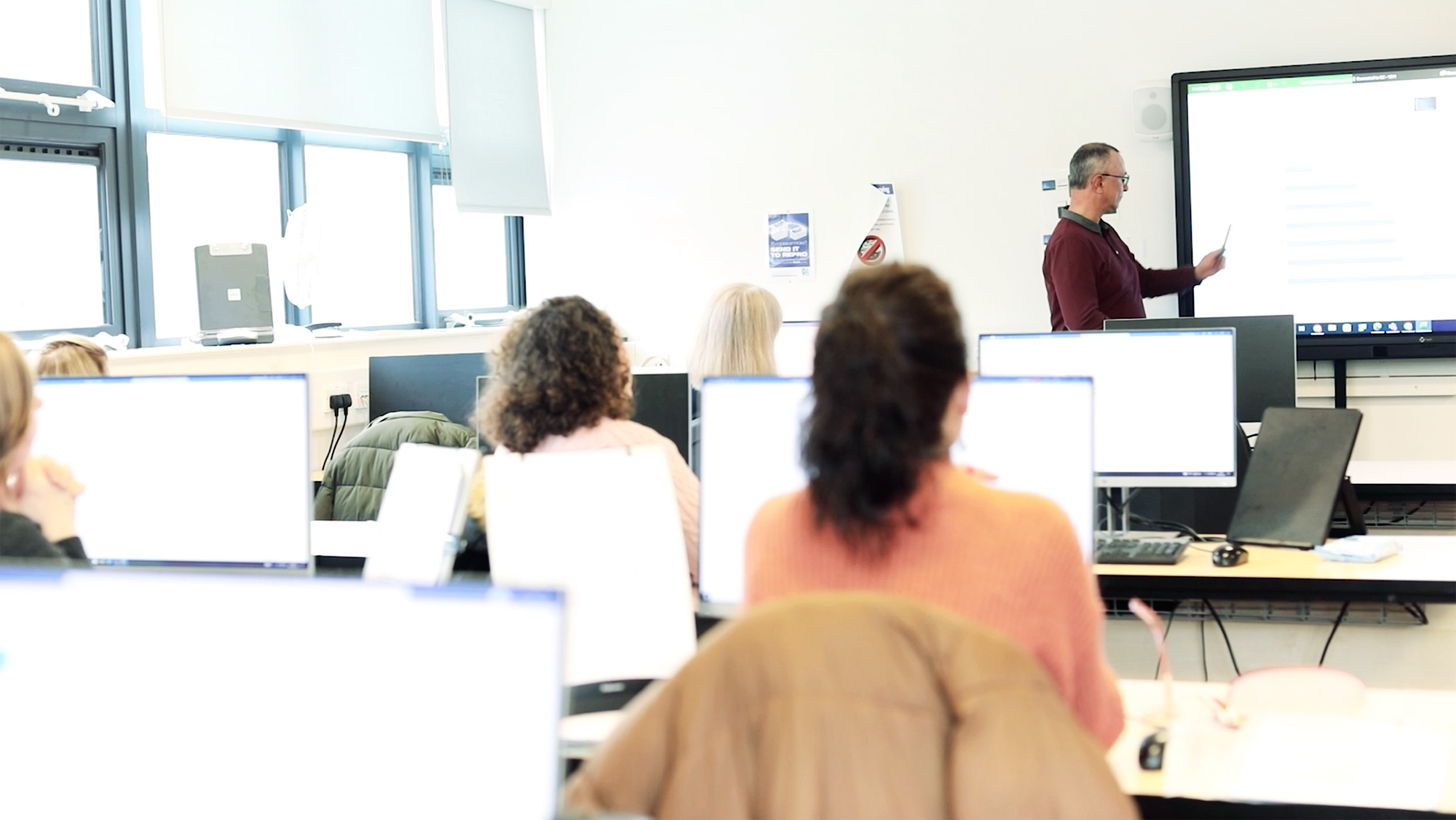 Students on computers watching lecturer using smart whiteboard