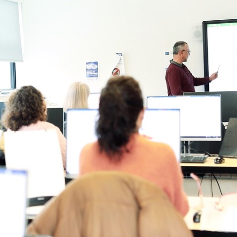 Students on computers watching lecturer using smart whiteboard