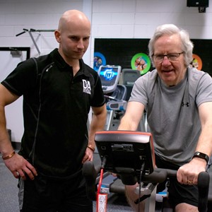 D&A fitness student working with an older member of the public on a stationary bike