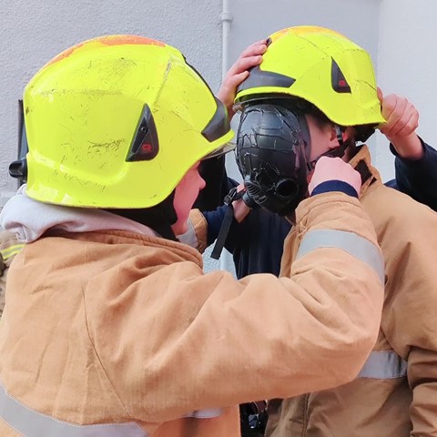 Students putting firefighter helmet on another student