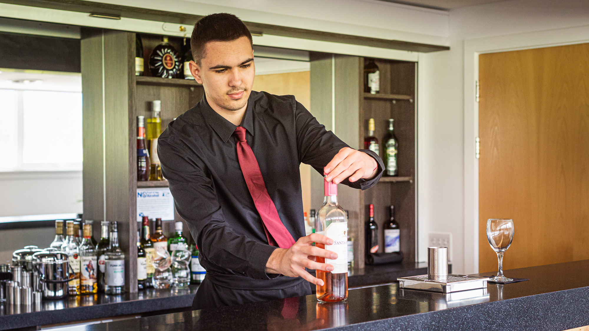 Student working behind bar screwing wine bottle lid on