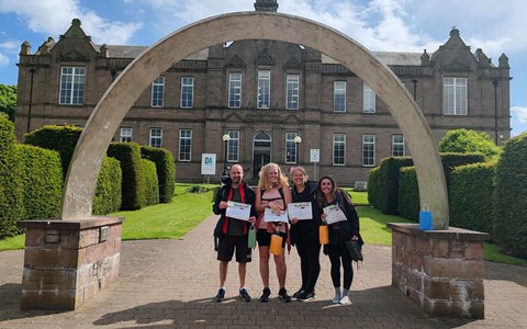 Four members of D&A staff at the Arbroath Campus after completing the cross campus challenge, smiling with their certificates