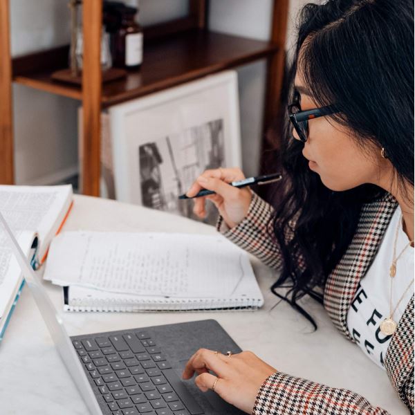 person at desk with laptop and writing on notepad