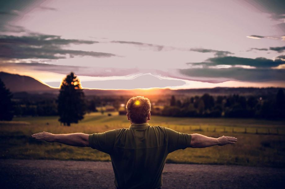 man standing with back to camera with arms out stretched and sun shining on him
