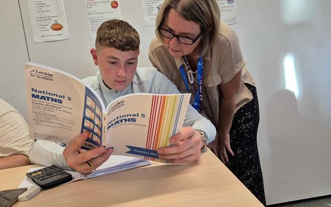 Young student gaining insights from a National 5 Maths Workbook along with support from a Lecturer