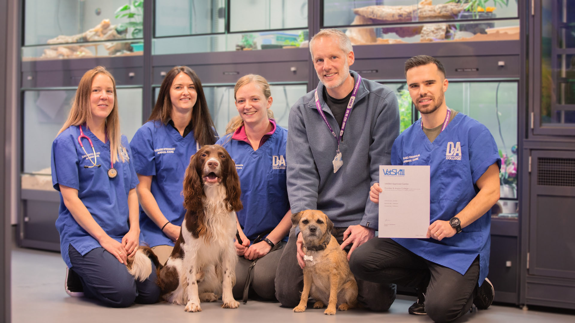 D&A Staff with their dogs proudly holding the VetSkill Centre Certification in front of six large aquariums )