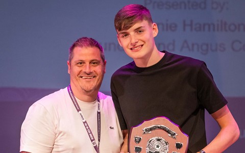 Student holding shield trophy standing next to lecturer