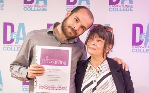 Student holding certificate with arm around parent in front of Dundee and Angus College backdrop