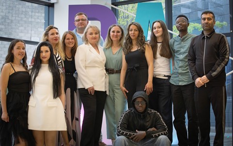A group of ESOL students standing in front of giant D&A letters at their graduation