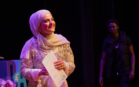 An ESOL student wearing a head scarf collecting her certificate on stage