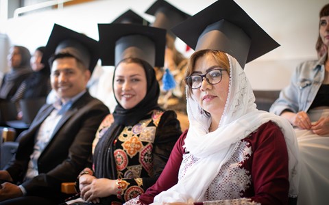ESOL students sitting wearing graduation caps that they made from cardboard