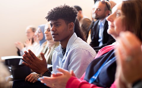 A close up image of a male ESOL student clapping in the audience of their graduation