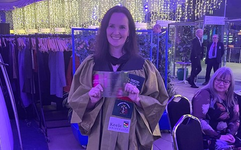 A person in a green gown stands at an awards event holding their award.