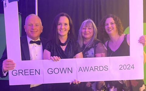 Four people standing together holding a large white frame with text that reads: '20th Anniversary,' 'UKRI UK Research and Innovation,' and 'GREEN GOWN AWARDS 2024