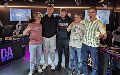 Five individuals celebrating in a gaming room, posing in front of computer stations with raised fists and thumbs up gestures.