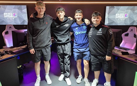 Four individuals standing together in a gaming room with purple LED lighting, smiling and posing with arms around each other in front of computer stations.