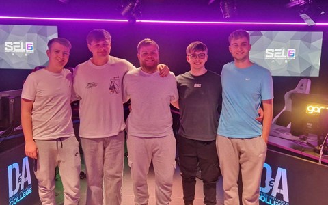 Five individuals posing together in a gaming room with purple LED lighting, standing in front of computer stations with arms around each other.