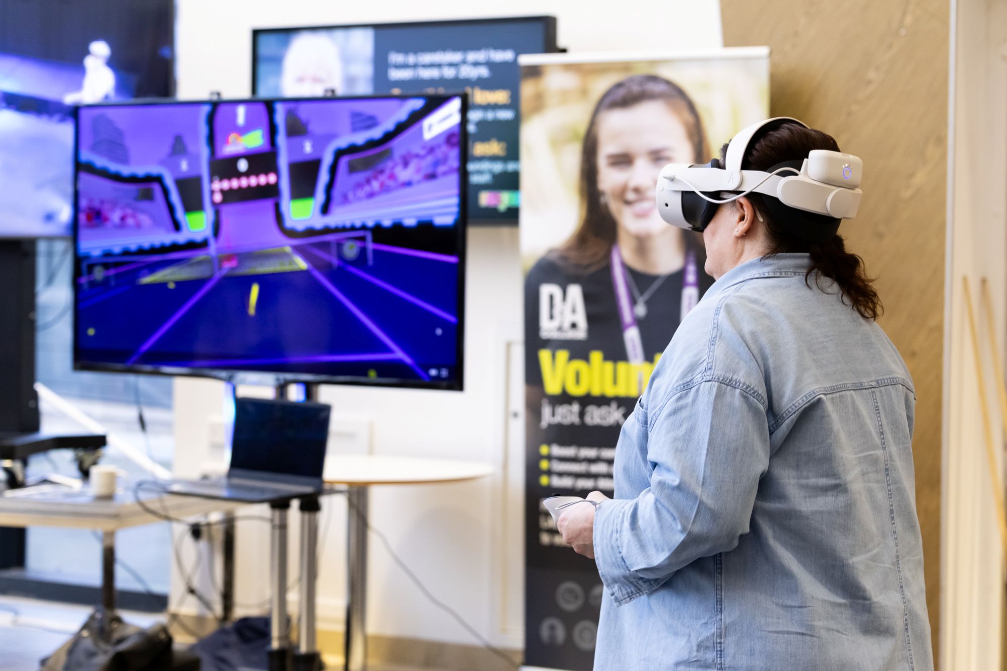 Person wearing a VR headset and holding controllers, interacting with a virtual tennis game displayed on a large monitor.