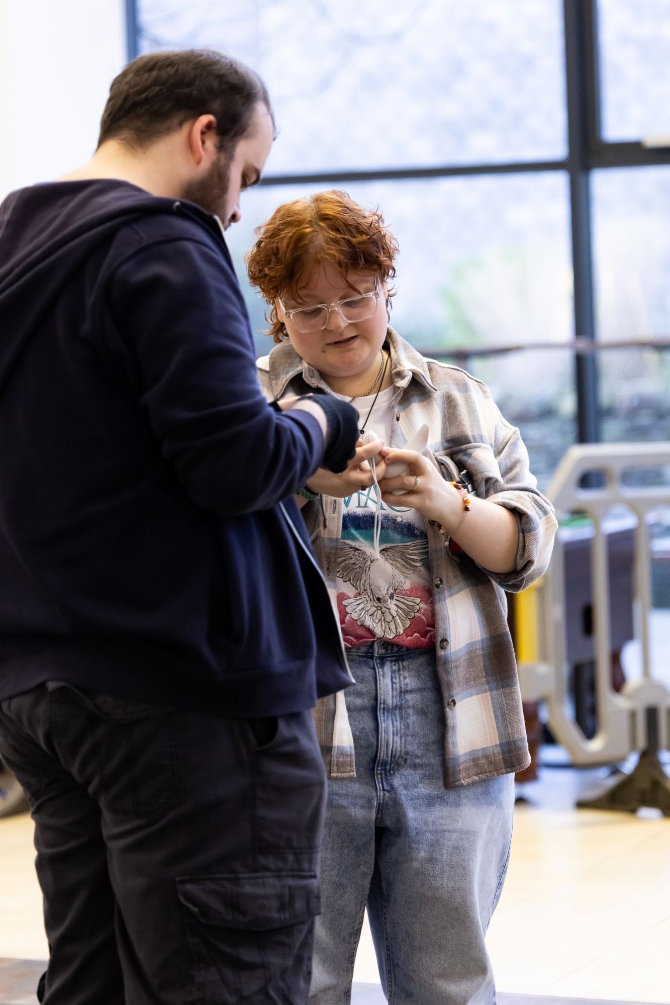 Two individuals standing close together, one handing or adjusting a small device for the other.