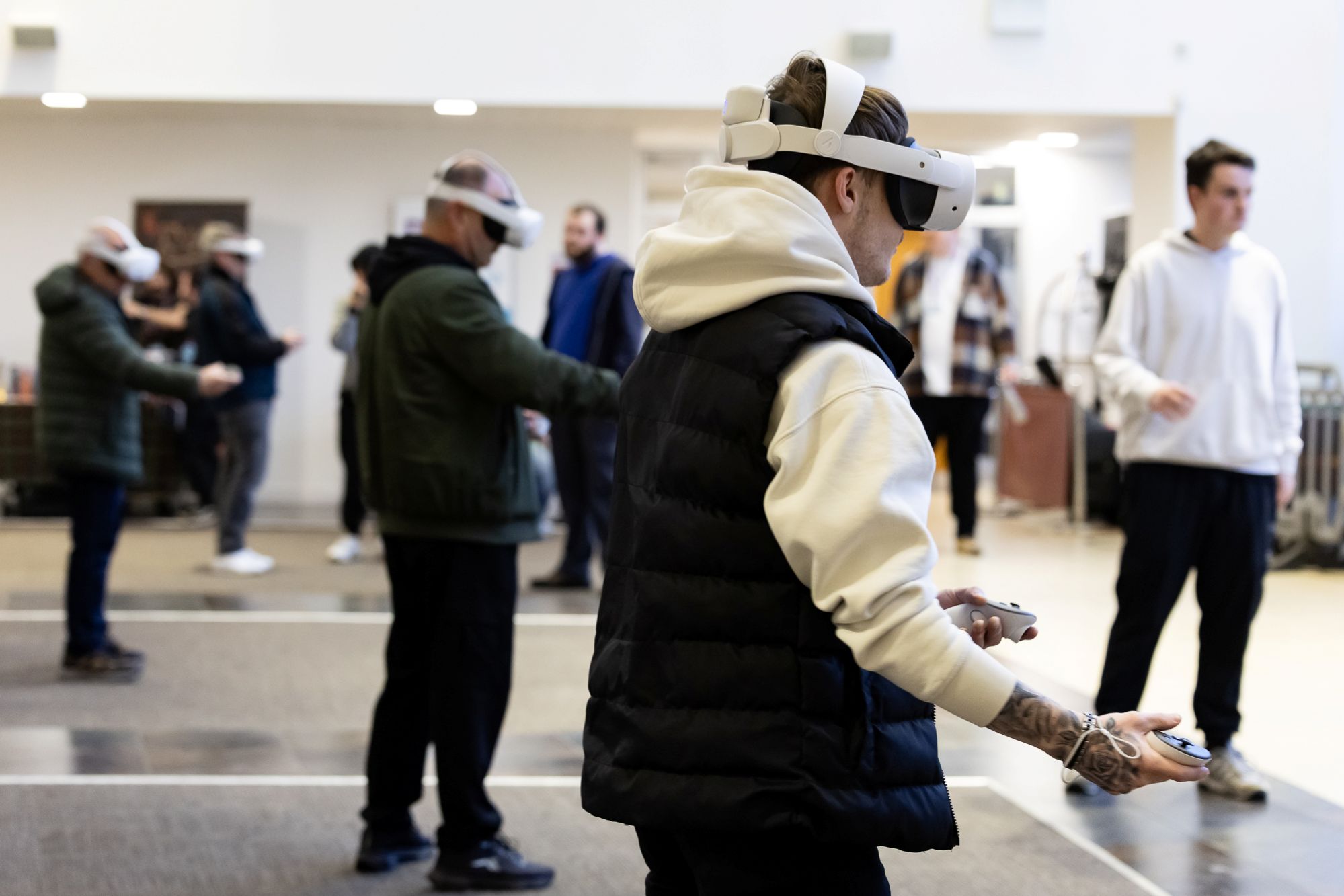 Several people in a spacious room wearing VR headsets and holding controllers, engaged in virtual activities.