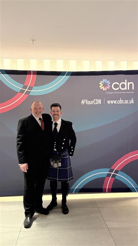 2 individuals dressed in formal attire stand in front of a backdrop labelled with CDN branding.
