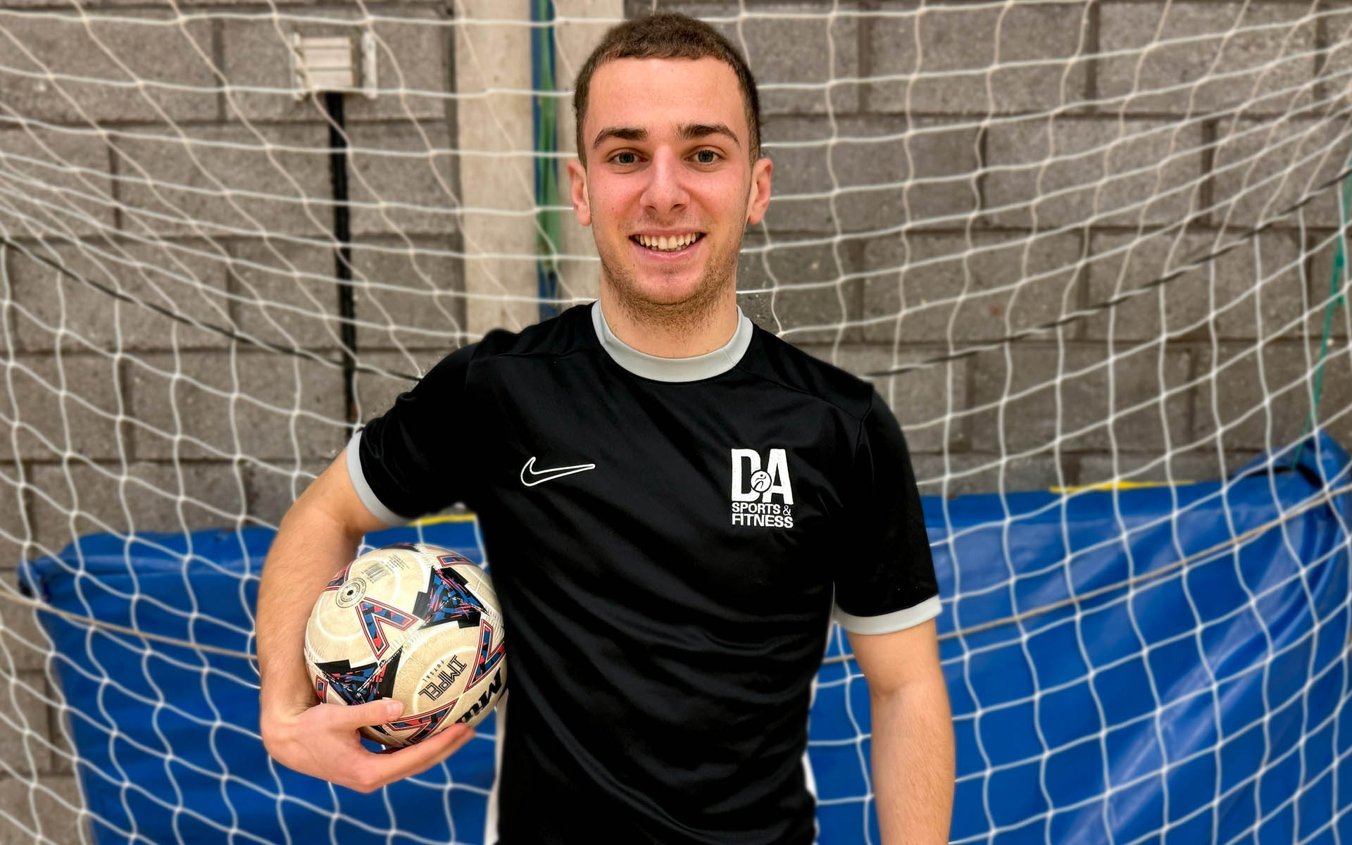 Sports student standing holding ball in front of goal)