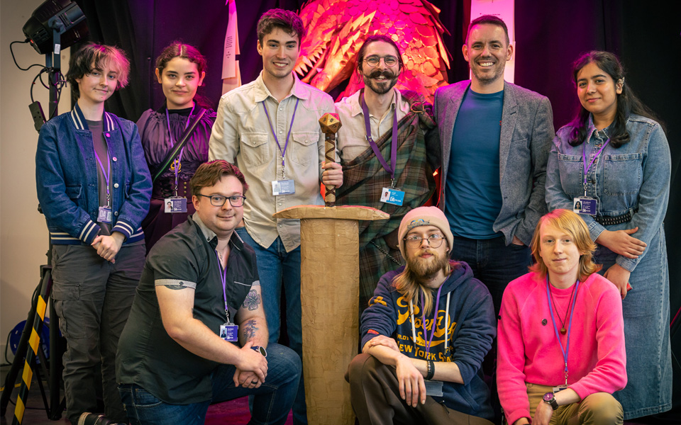 Group photo of volunteer students and member of staff standing in front of dragon and posing with sword