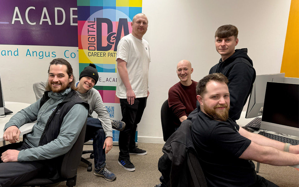 Ex computing students gathered around computer smiling at camera