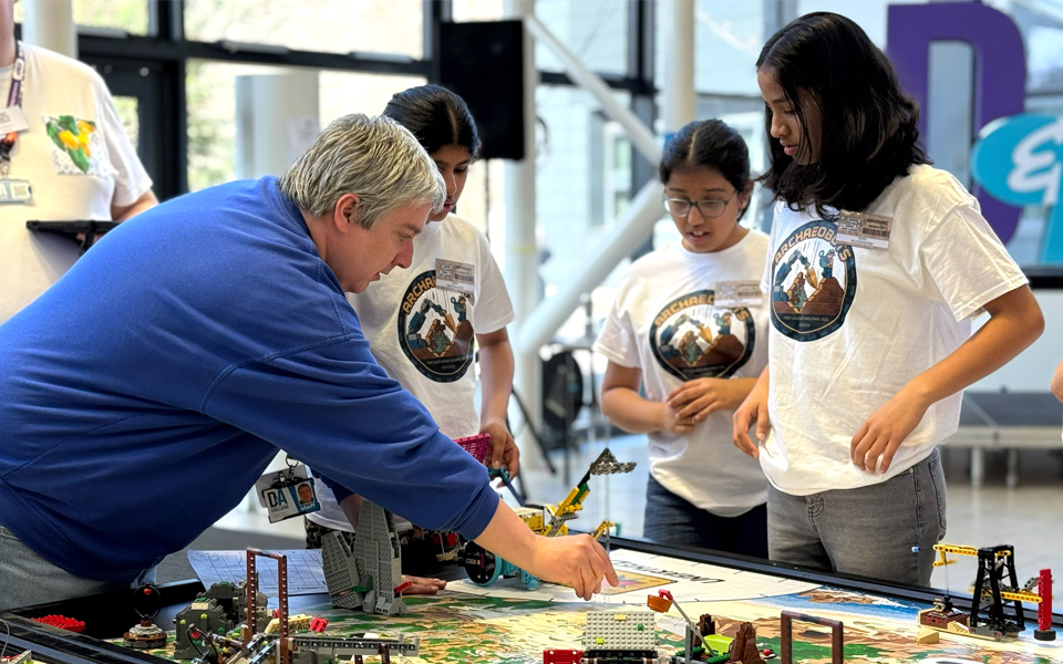 Lecturer with group of school pupils arranging lego robot