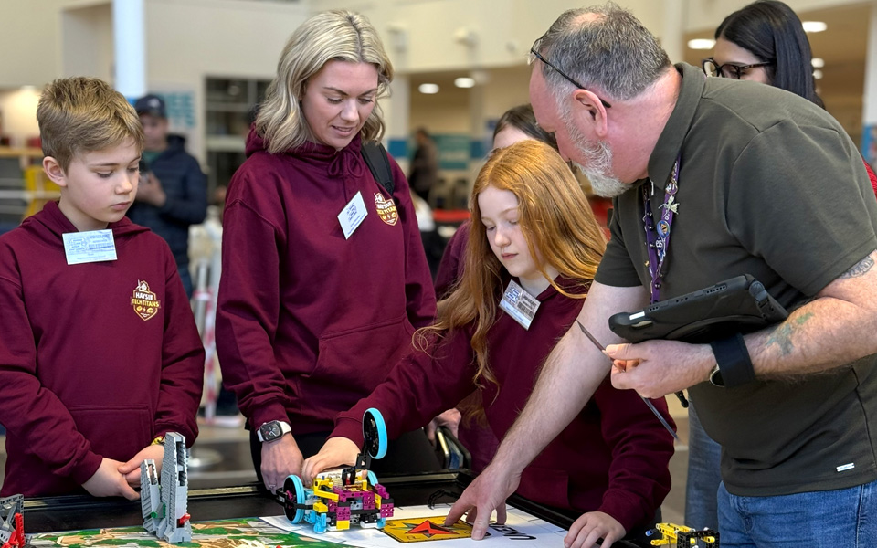 School pupils with teacher and lecturer looking at lego robot