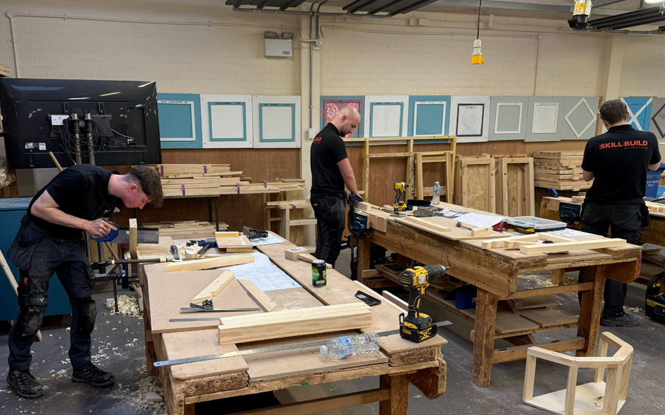 Three carpentry students working at benches in workshop