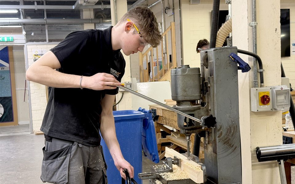 Student with goggles on in construction workshop operating machinery