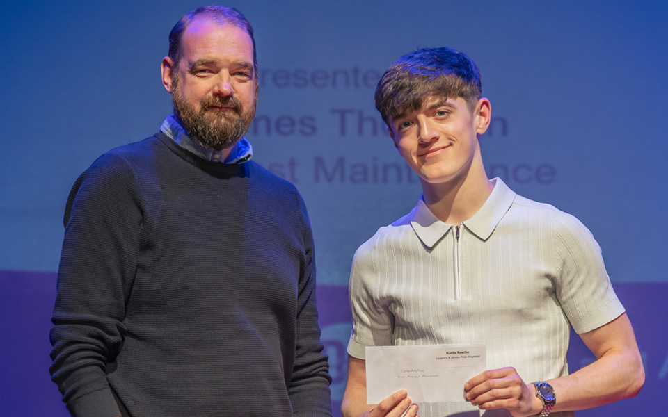 Student on stage with prizegiving sponsor holding envelope prize