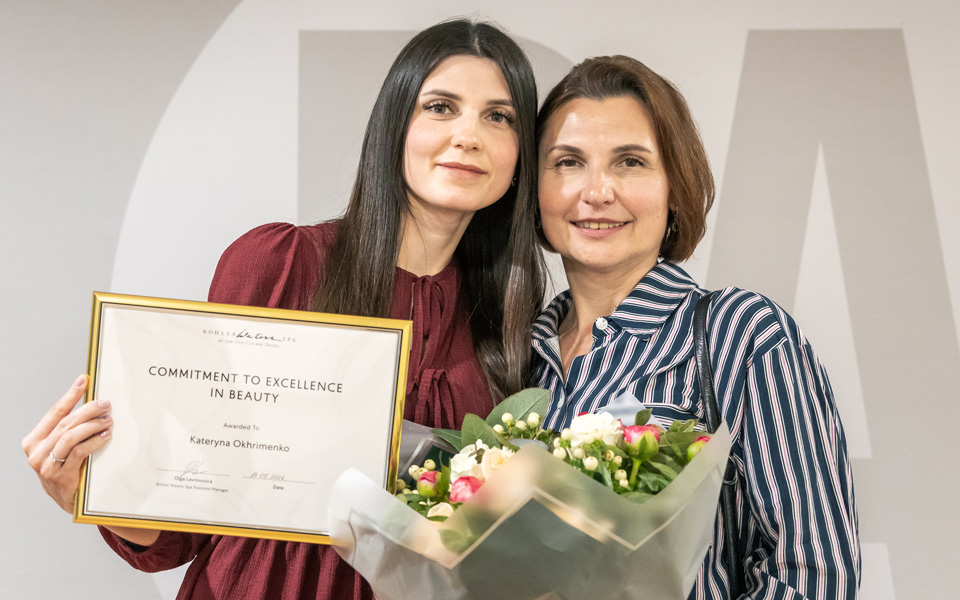Student prizewinner holding framed certificate with guest holding flowers