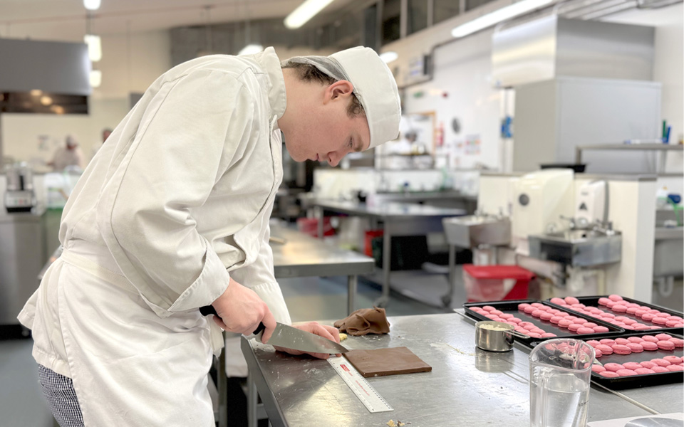 Student cutting icing for cake in kitchen