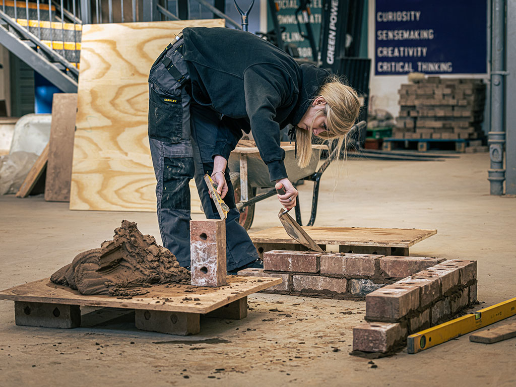Student applying cement to small bricklaying project