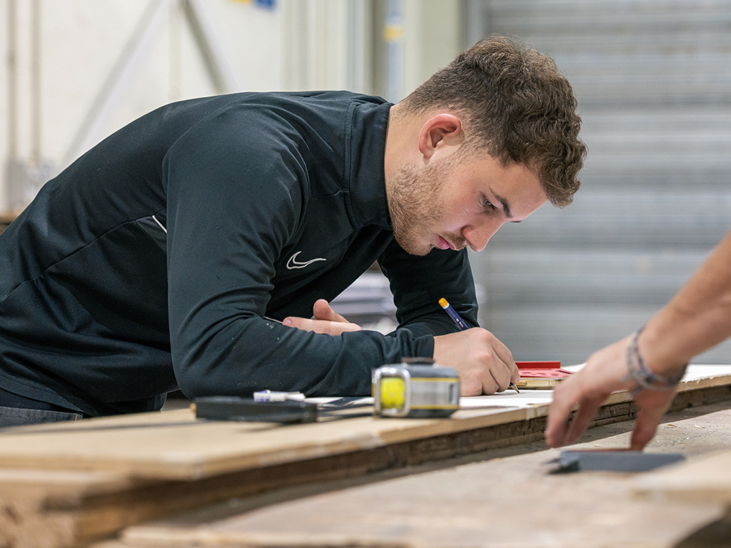 Joinery student sketches plans on a wooden board