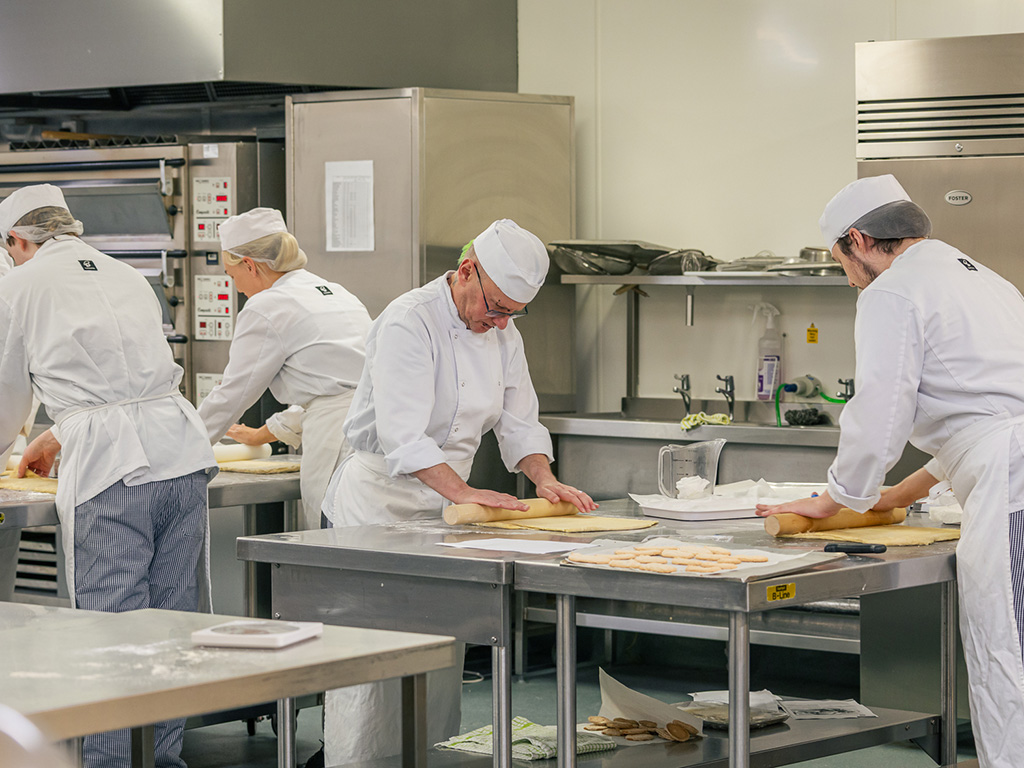 Cookery students rolling out dough in a bakery class