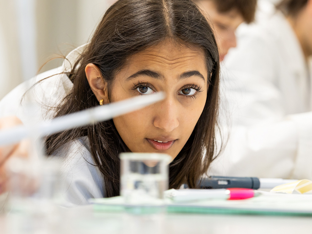 Student in lab-coat measuring in a beaker