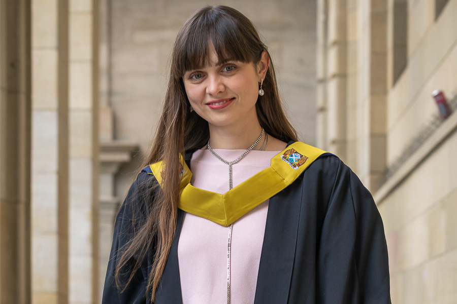 Student smiling outside Caird Hall in graduation robe