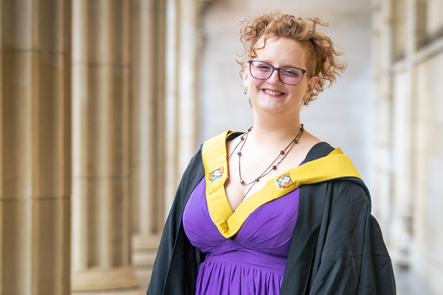 Student smiling outside Caird Hall in graduation robe
